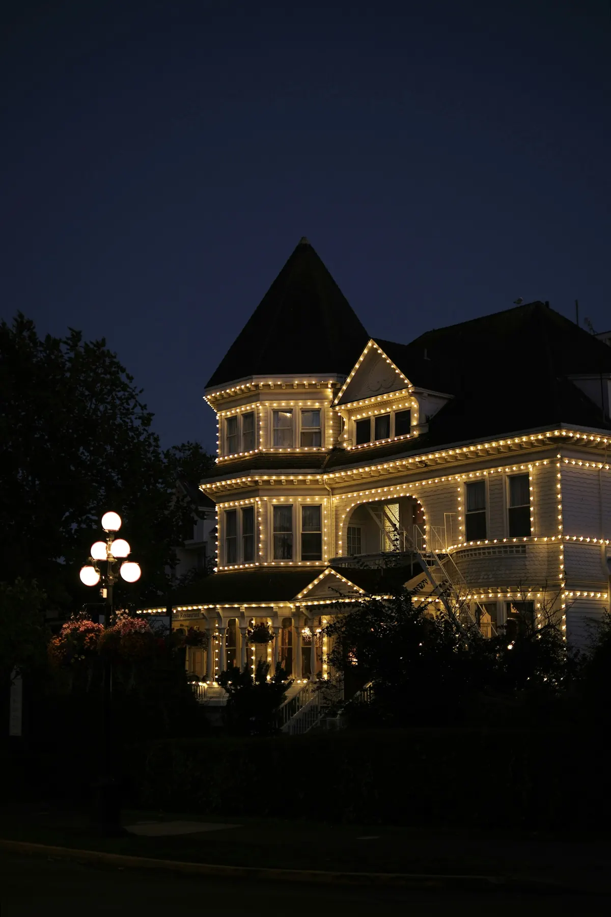 Victorian home outlined in Christmas lights at dusk