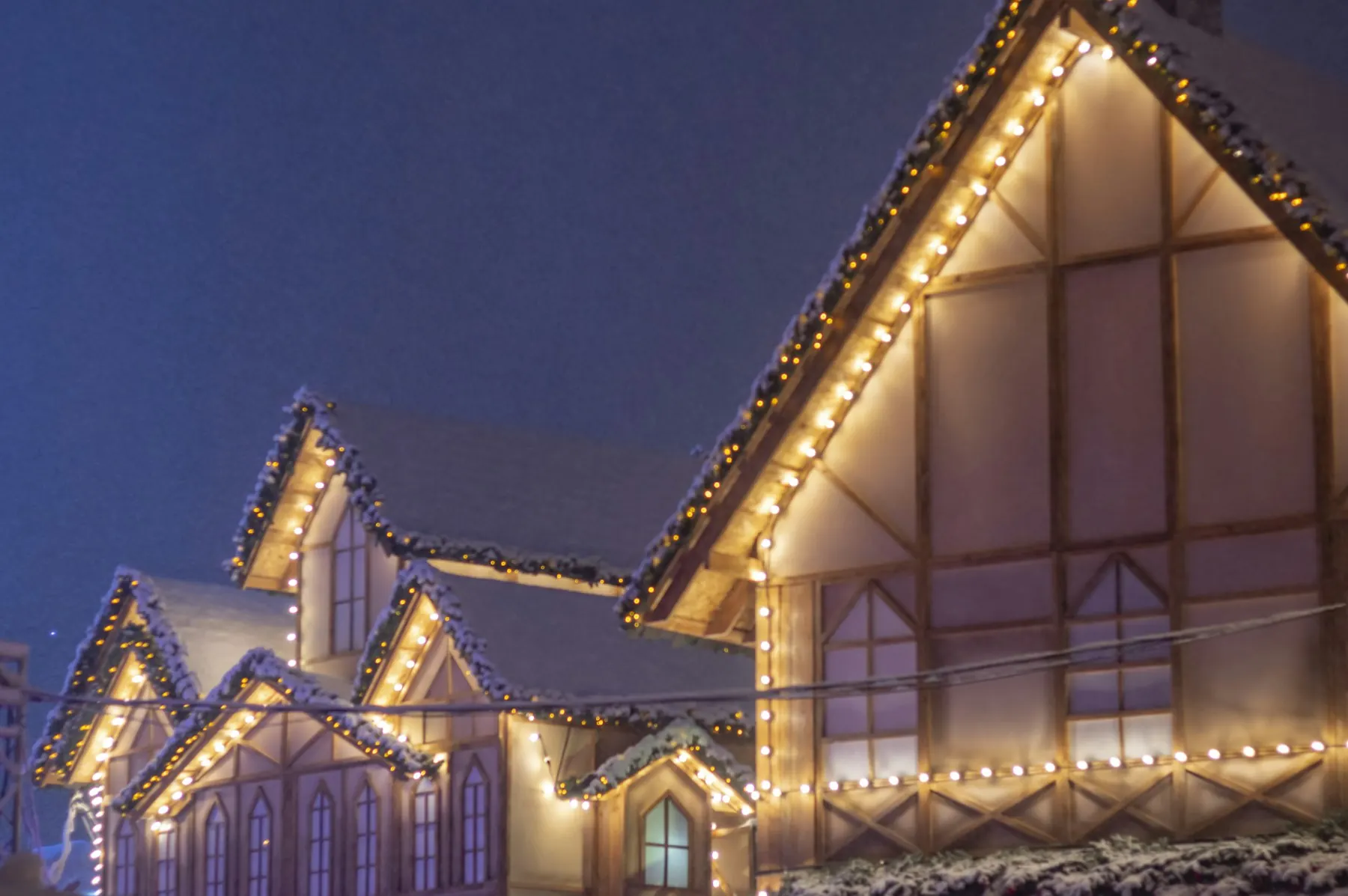 Two-story home with warm white Christmas lights along every roofline at dusk